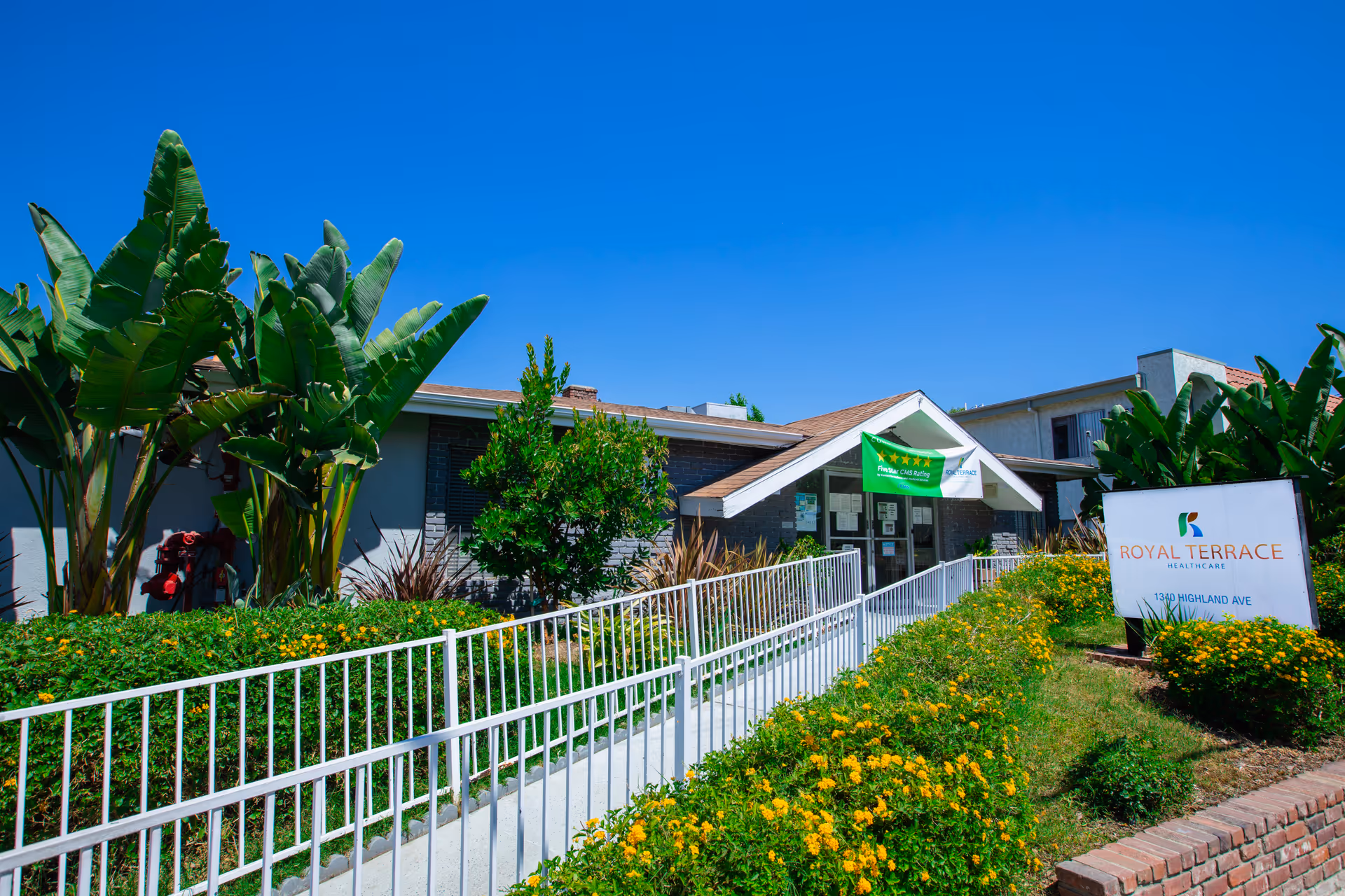 Front entrance of the Royal Terrace Health Care building with a ramp, landscaping and a sign.