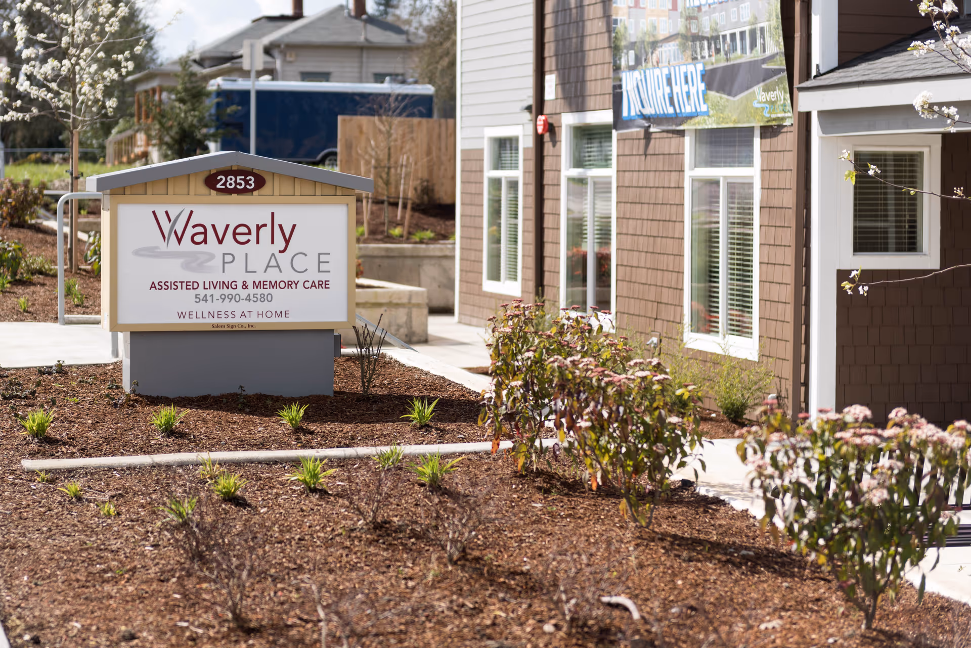 Outdoor view of Waverly Place assisted living and memory care facility sign with landscaping and part of the building exterior visible in the background.
