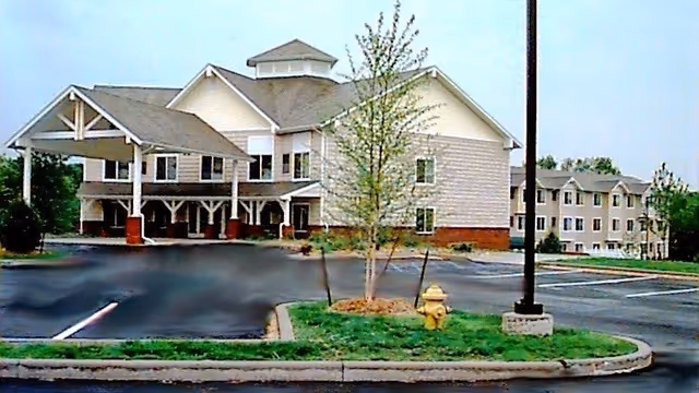 Exterior view of St. Andrew's Apartments at Kirksville, showing a multi-story building with a covered entrance, parking lot, a small landscaped area with a tree and a yellow fire hydrant, and a street lamp.