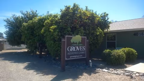 Front view of Groves Assisted Living sign with trees and building entrance.