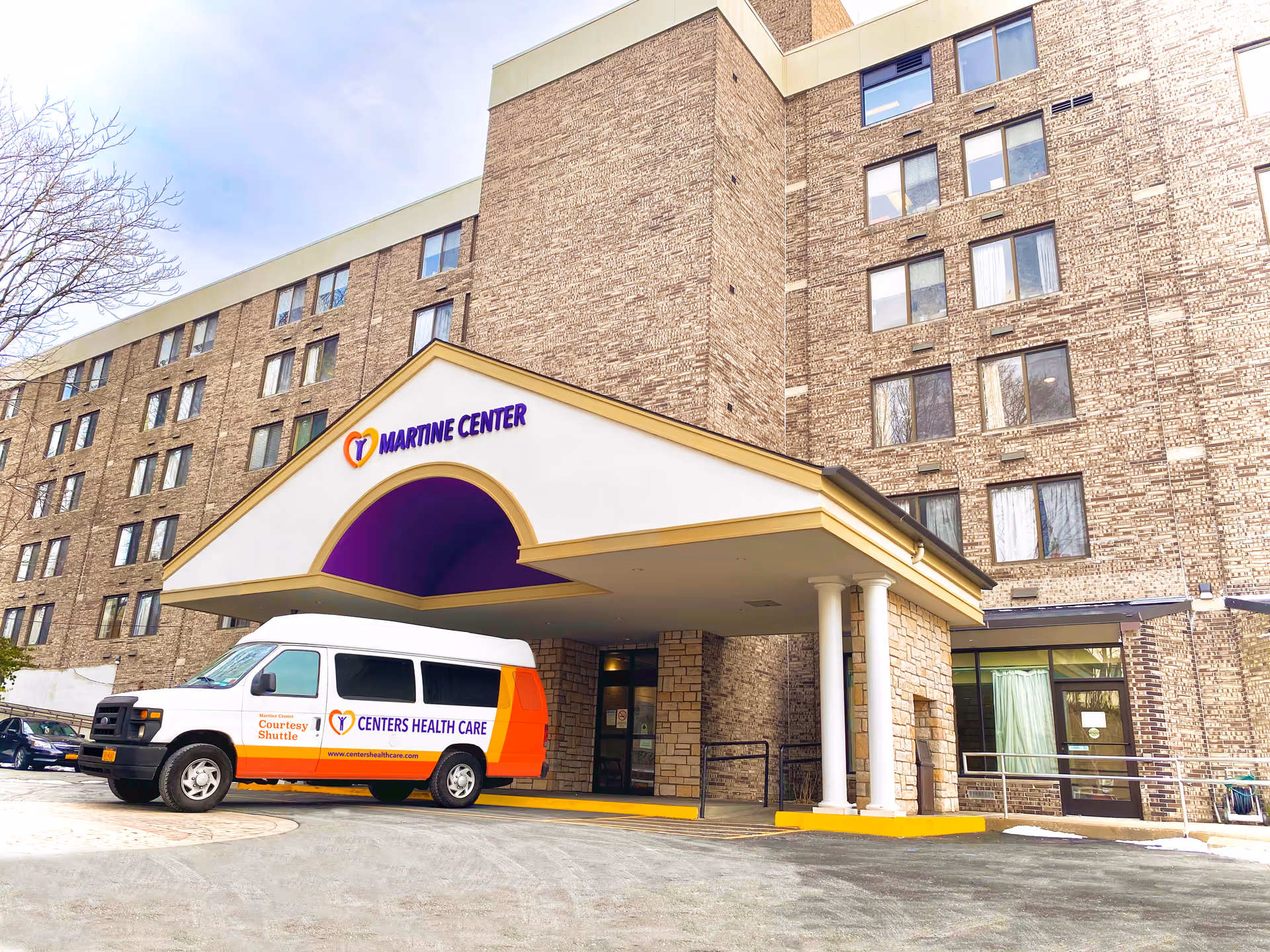 Exterior view of the Martine Center for Rehabilitation and Nursing building showing a multi-story brick facade with numerous windows. A white and orange courtesy shuttle van labeled 'Centers Health Care' is parked under a covered entrance with white columns and a purple accent inside the arch.