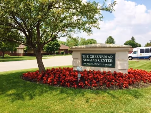 Exterior view of The Greenbriar Nursing Center sign surrounded by red flowers and trees.