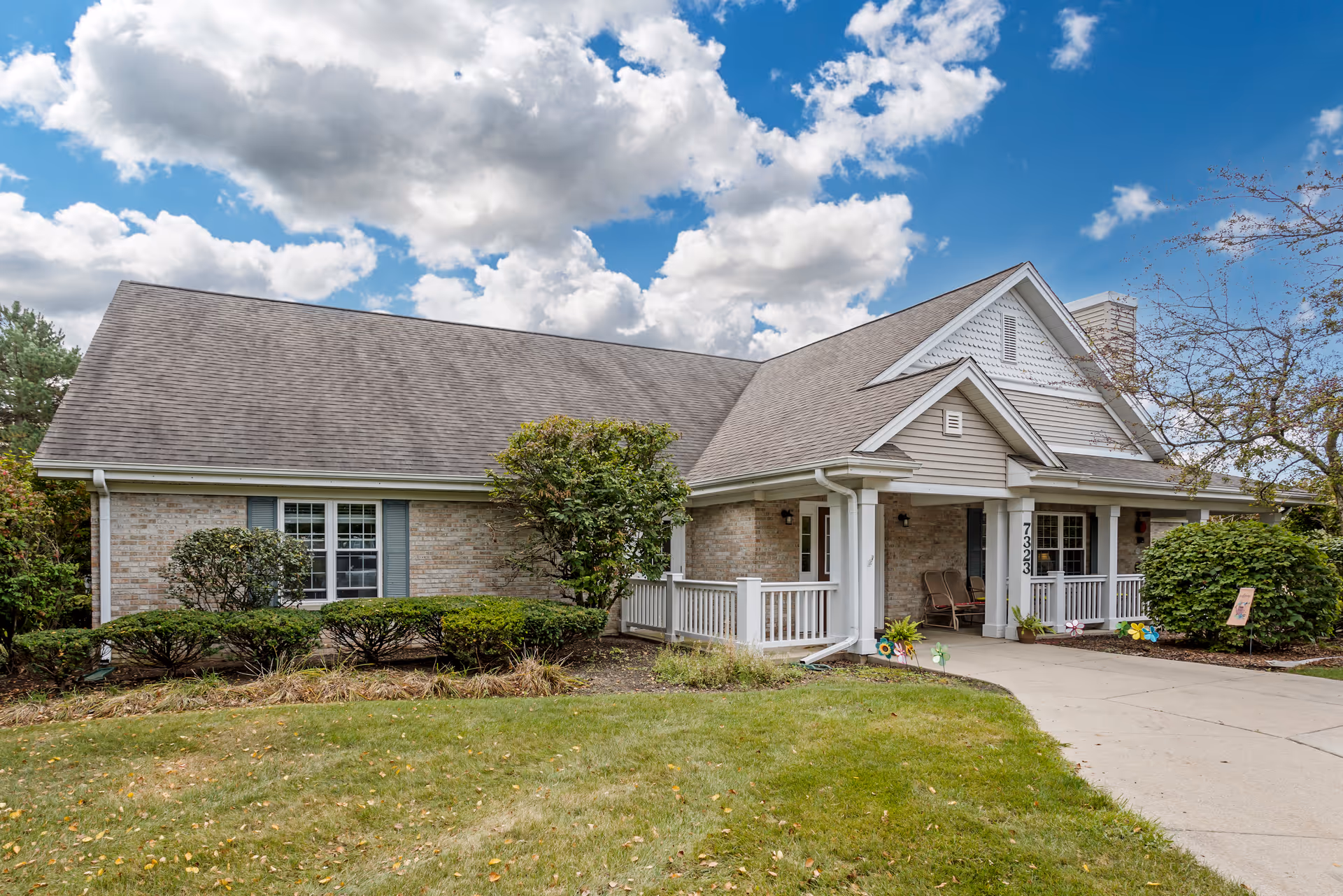 Single-story brick and siding building with a covered front porch, driveway, and landscaped lawn under a partly cloudy sky.