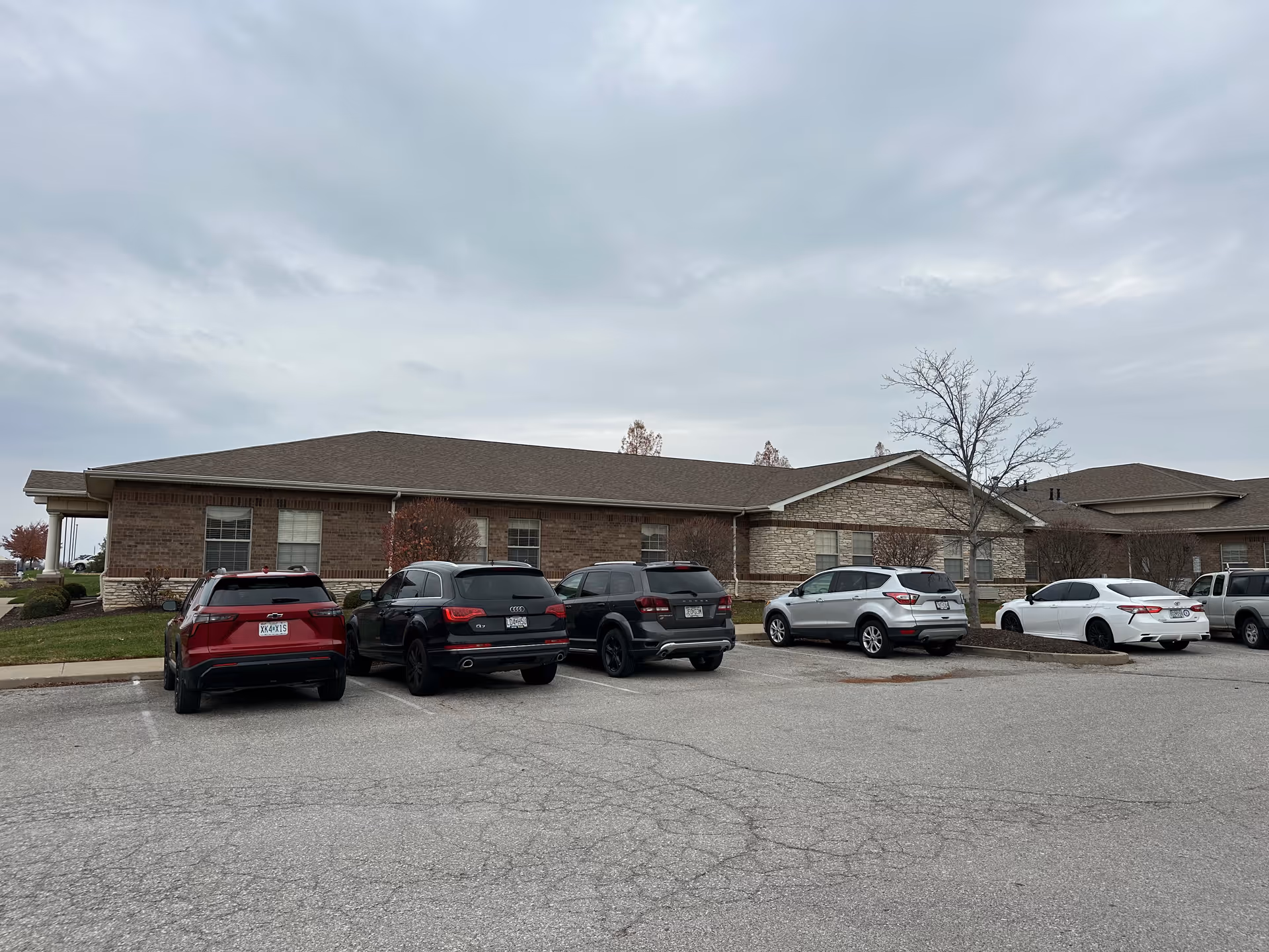 Single-story brick building with several cars parked in front in a parking lot under an overcast sky.