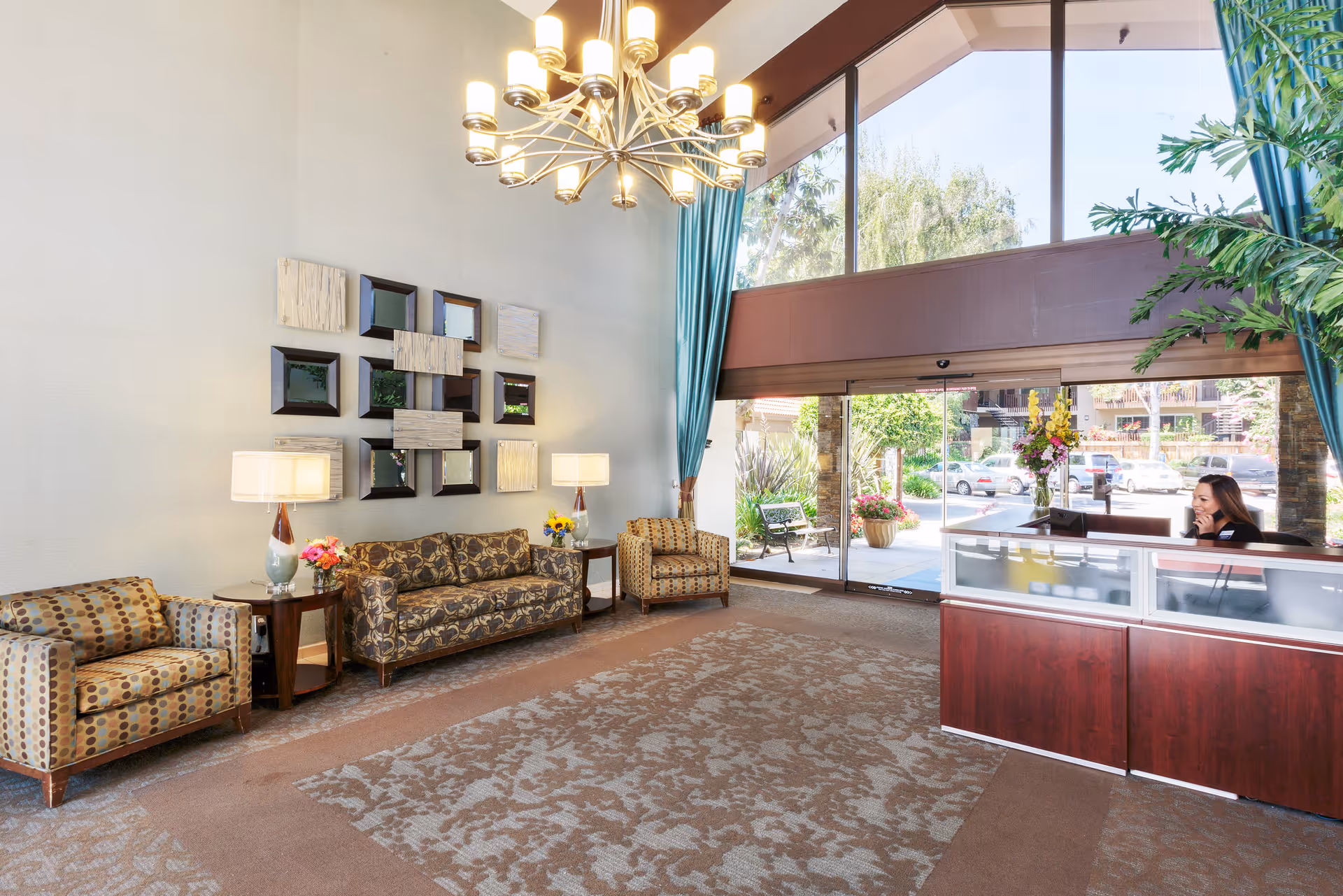 Spacious lobby with seating, a chandelier, and a reception desk by large windows and the entrance.