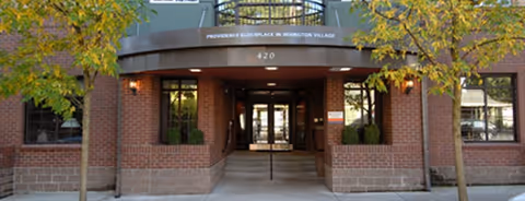 Brick building entrance with a covered walkway, trees, and Providence Elder Place Irvington Village signage.