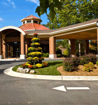 Entrance of a brick building with a covered driveway and a landscaped area featuring a tiered topiary and flowers under a clear blue sky.
