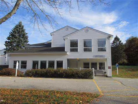 White two-story building with large windows, a ramped entrance, and a parking lot.
