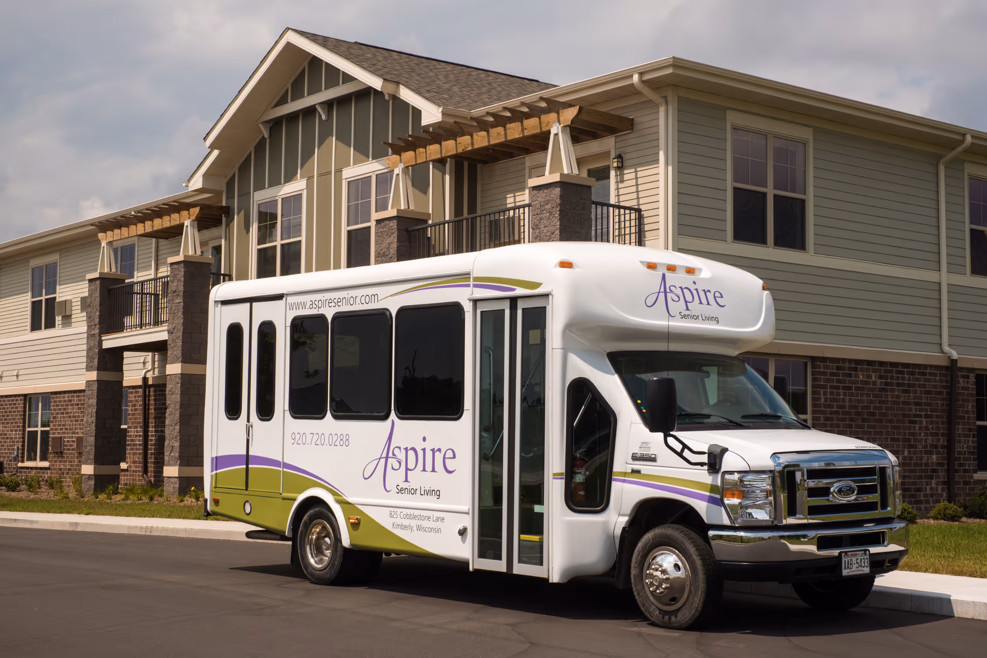A white Aspire Senior Living shuttle bus parked in front of a two-story senior living building.