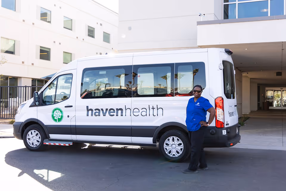 A Haven Health shuttle van parked outside a senior living facility with a staff member in blue standing by the rear door.