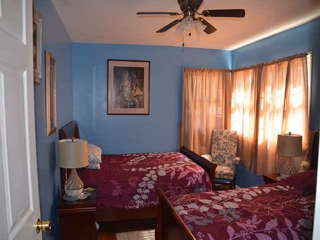 Small bedroom with two twin beds, blue walls, floral bedding, nightstands, and a curtained window.