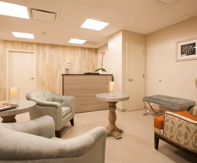A cozy reception area with upholstered chairs, side tables, and a front desk in neutral tones.
