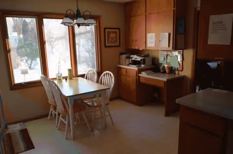 Dining area with a wooden table, white chairs, and a large window.
