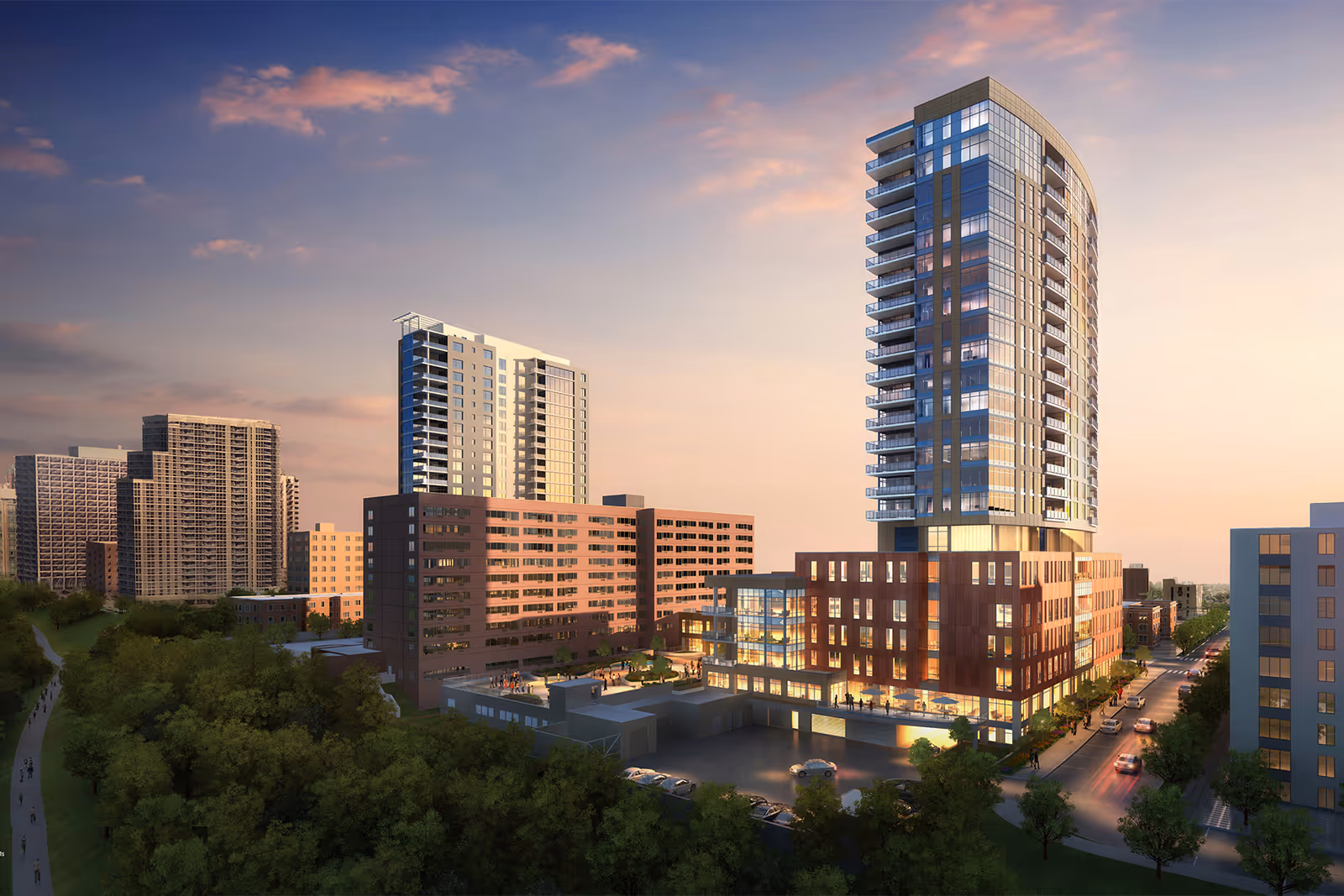 A modern high-rise building complex at sunset with glass and brick exterior, surrounded by trees and other buildings in an urban setting.