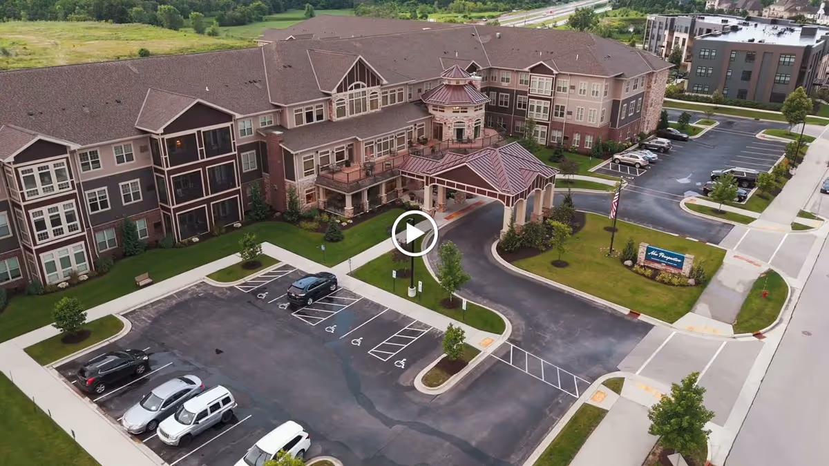 Aerial view of New Perspective Senior Living | Franklin facility showing a large multi-story building with a covered entrance, surrounding parking lot with several cars, landscaped green areas, and a sign near the entrance.
