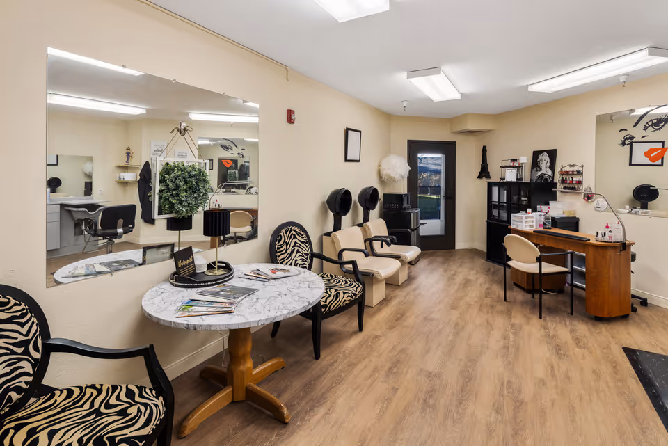 Interior salon area with zebra-print chairs, a marble-top waiting table, hair dryers, a manicure station and large wall mirrors.