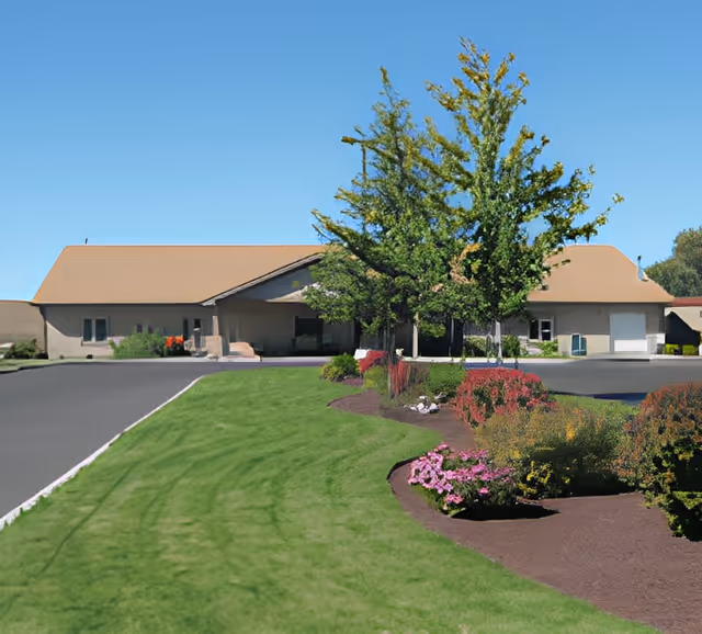 Front exterior of a single-story senior care facility with a pitched roof, landscaped lawn, and driveway.