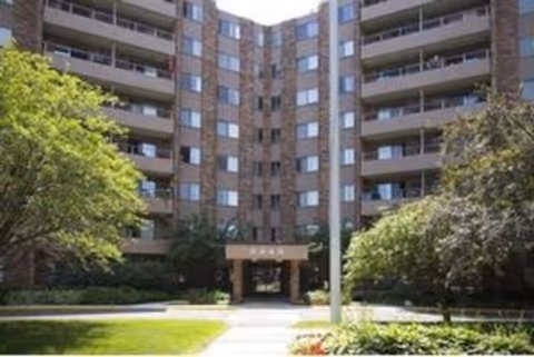 Brick senior living building with central entrance and surrounding trees.