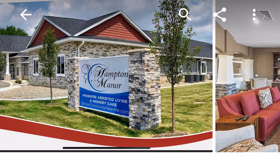Exterior view of Hampton Manor assisted living building with a stone sign on a grassy lawn and a glimpse of a furnished living room at the right edge.
