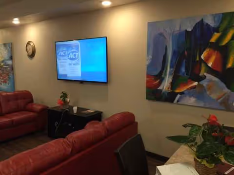 Red leather couches surround a wall-mounted TV in a modern senior living lounge with abstract art.