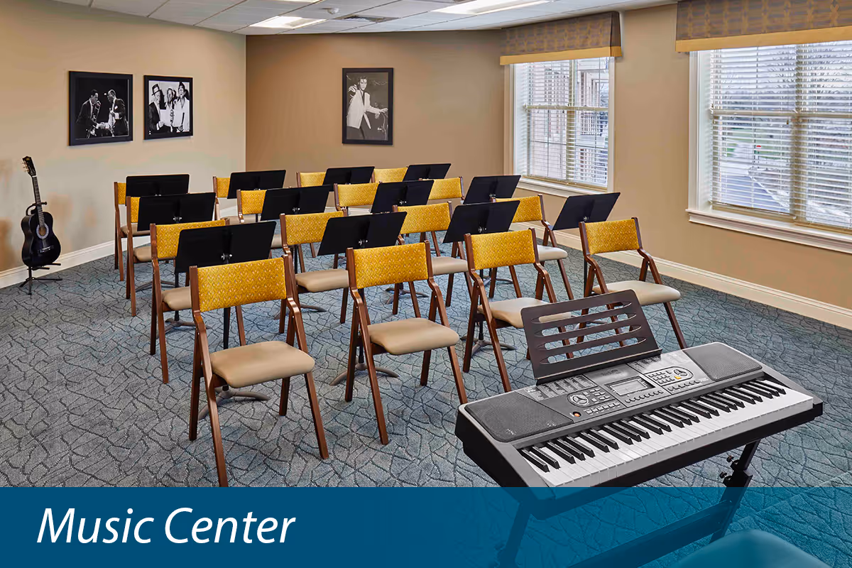 Rows of chairs with music stands, a keyboard and a guitar in a bright activity room with windows and framed photos.