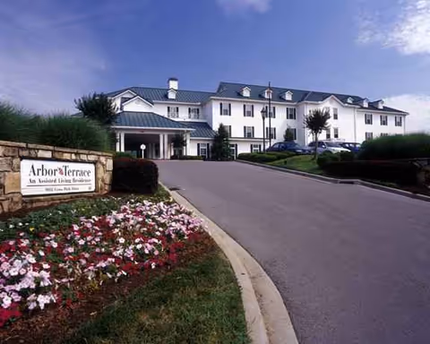 White multi-story senior living facility with curved driveway and colorful flower beds.
