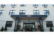 Entrance of a multi-story building with a canopy showing the number 353 and glass doors below.