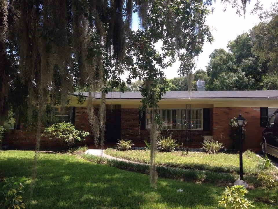 Single-story brick building with a front lawn, trees draped in Spanish moss, and a walkway to the entrance.