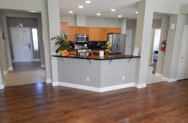 Open kitchen with a black granite-topped island, wooden cabinets, stainless steel appliances, and hardwood floors.
