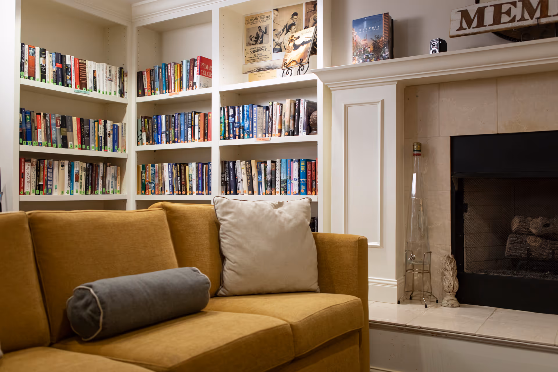Cozy living room with a mustard-yellow sofa in front of built-in bookshelves and a fireplace.