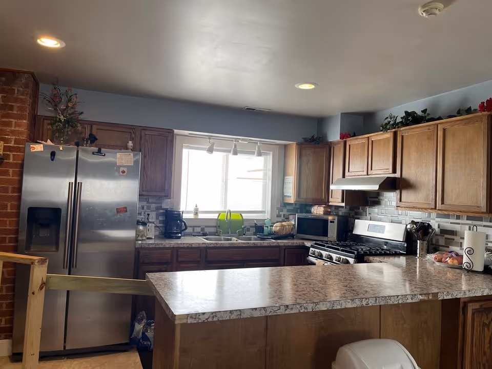 Kitchen with wooden cabinets, stainless steel refrigerator and stove, a large island countertop, and a window above the sink.
