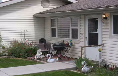 Exterior view of a house with a small patio, chairs, and garden decorations.