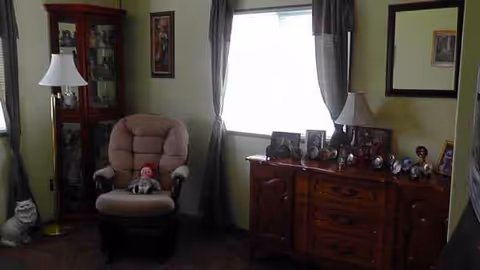 A cozy living room with a recliner, lamps, curtains, and a dresser with photos.