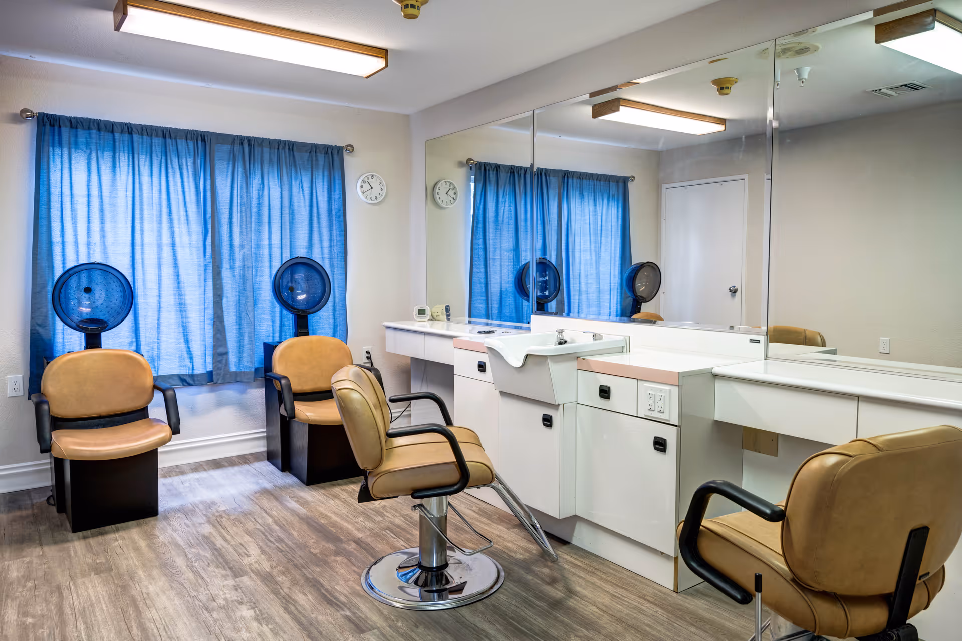 A bright interior salon with styling chairs, hooded hair dryers, a sink, and a large mirror.