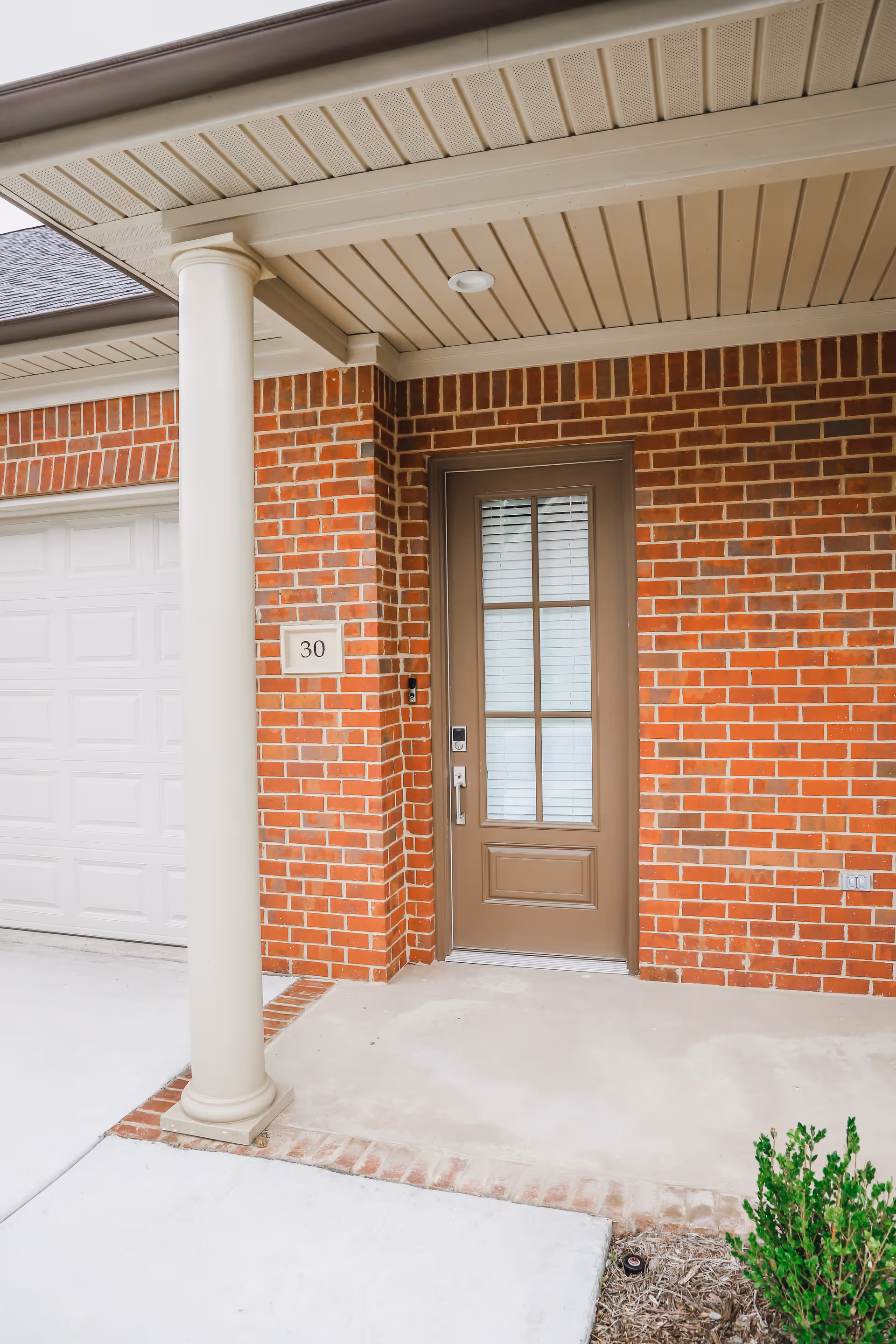 Front entry of a red brick home with a brown glass-paneled door, a column, and house number 30 next to a garage door.