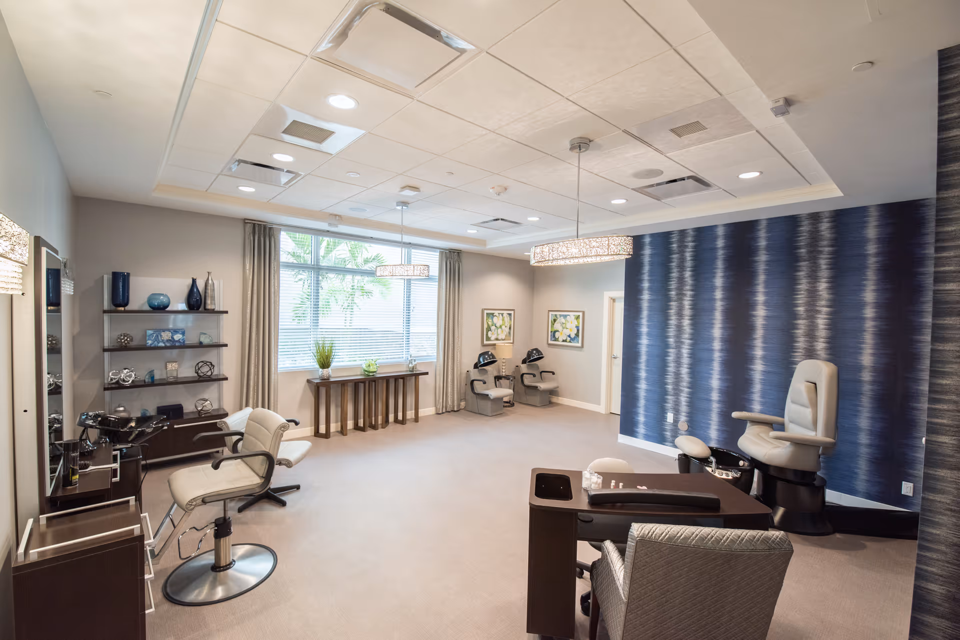 Bright modern salon/spa room with styling chairs, manicure/pedicure stations, shelving, and a large window.