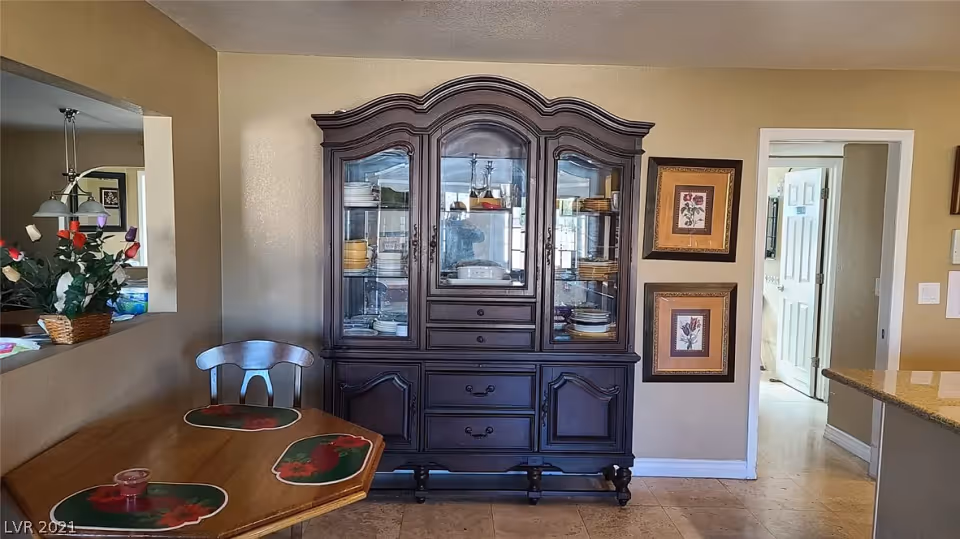 Dining area showing a dark wooden china cabinet against a wall, a wooden table with placemats and chair, and doorways to adjacent rooms.