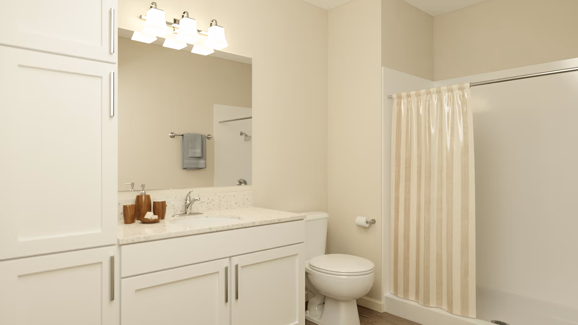 A clean and modern bathroom featuring a white vanity with a speckled countertop, a large mirror with three light fixtures above it, a toilet, and a shower with a beige and white striped curtain.