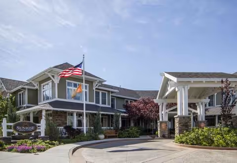 Sunrise of Sandy facility exterior with a covered entrance, flagpole, and landscaped driveway.