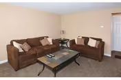 A living room with two brown sofas, patterned throw pillows, a rectangular coffee table, a side table with lamp, beige walls and carpet.