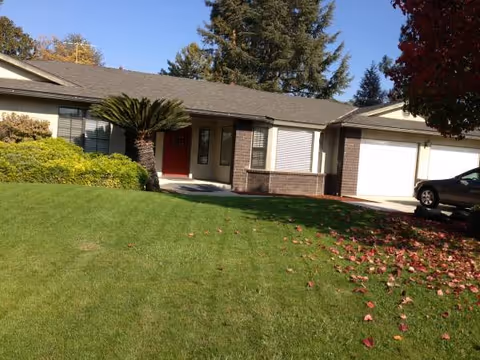 Front exterior of a single-story Serenity Living facility with a grassy lawn and driveway.