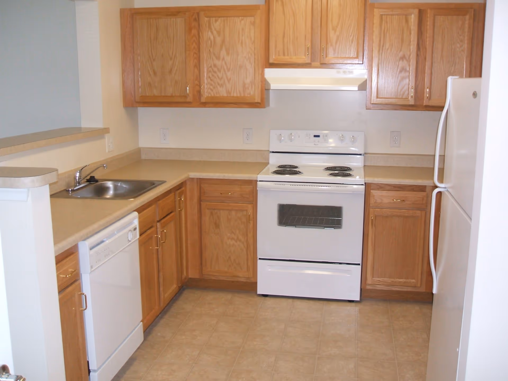 Small kitchen with a white stove, refrigerator, dishwasher, sink, and oak cabinets.