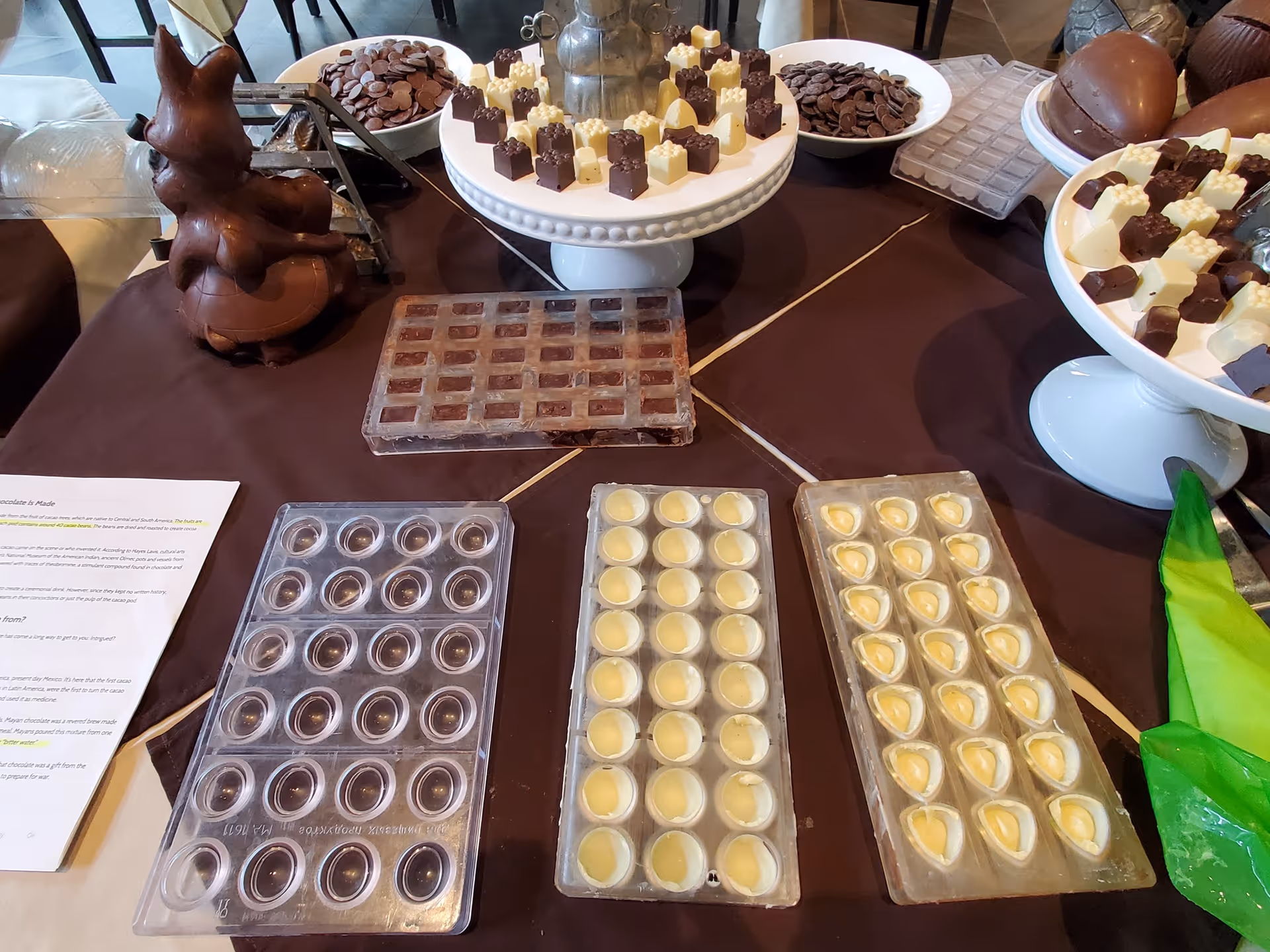 Table display of chocolate molds and assorted white and dark chocolate pieces on platters.