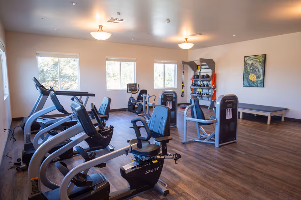Bright interior fitness room with treadmills, stationary bikes, and weight machines.