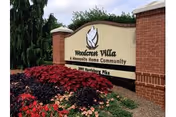 Brick and stone entrance sign reading 'Woodcrest Villa A Mennonite Home Community' surrounded by landscaping and flowers.