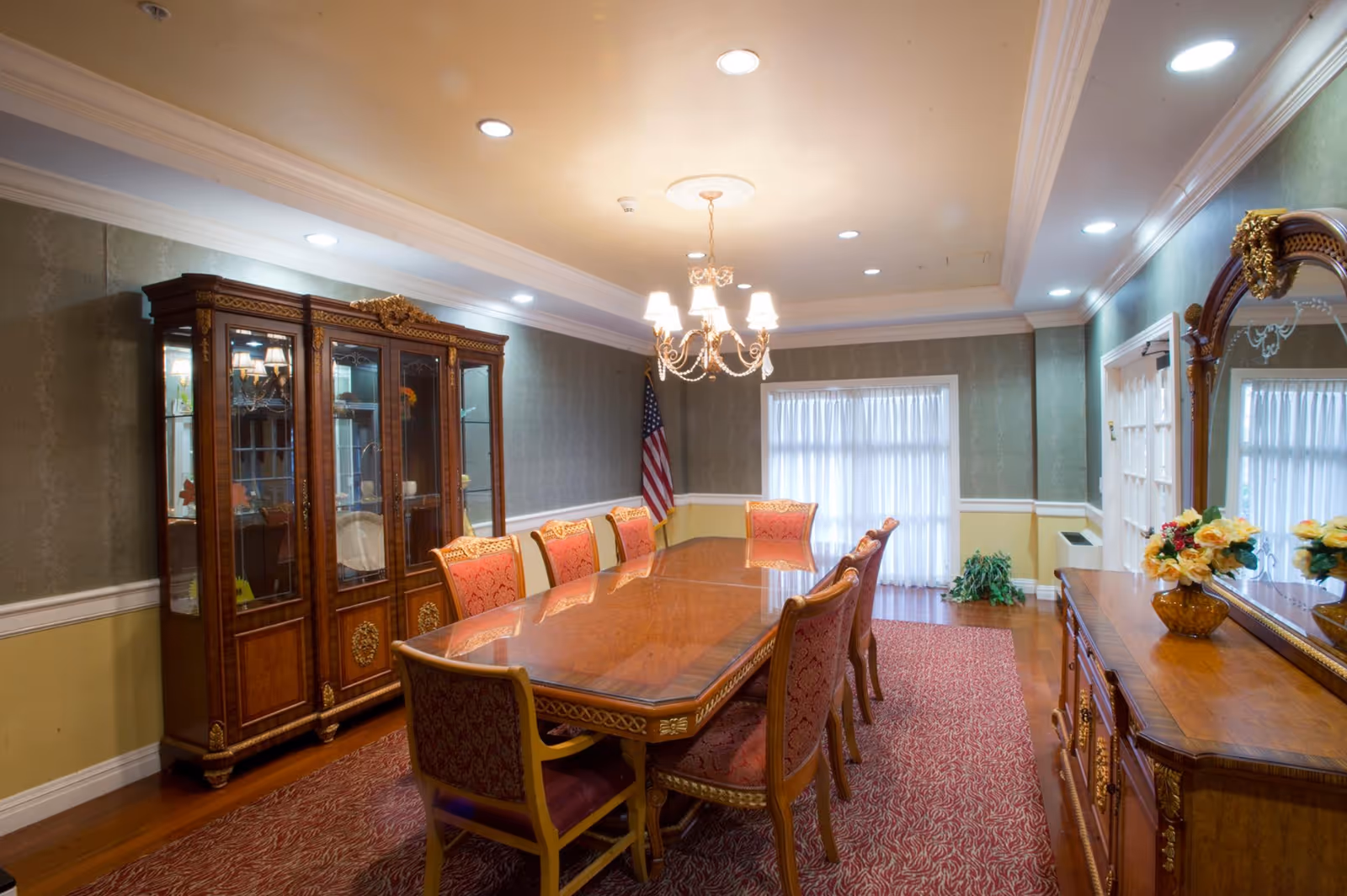 Formal dining room with a long wooden table, upholstered chairs, chandelier, china cabinet and decorative mirror.