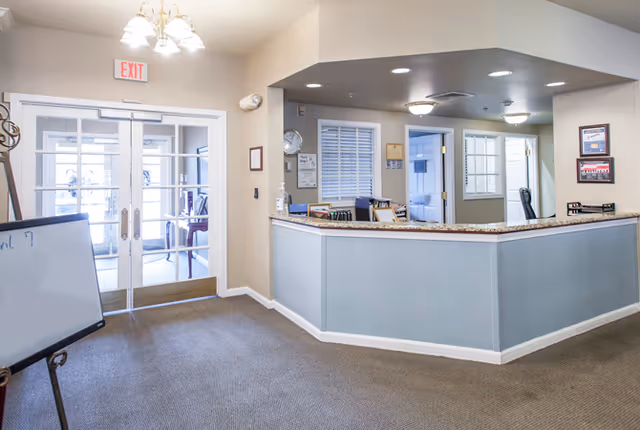Lobby reception area with a curved front desk, double glass entrance doors, and an exit sign.