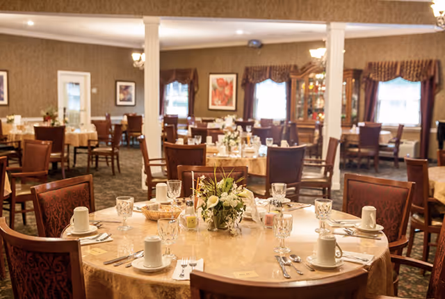 Elegant senior living dining room with round tables set for a meal and floral centerpieces.