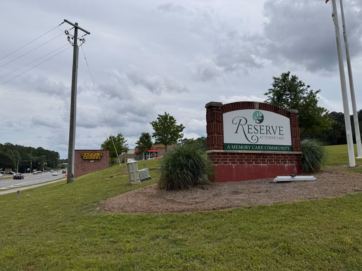 Brick entrance sign for Reserve at Towne Lake memory care community by a roadside under a cloudy sky.