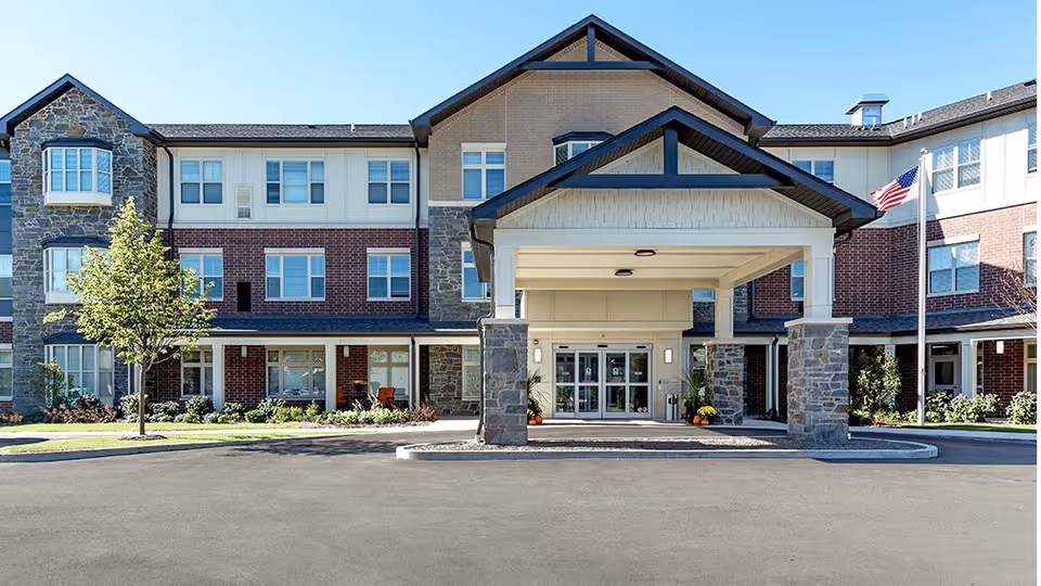 Front entrance of the Sunrise of Prospect Heights senior living building featuring a covered porte-cochère and an American flag.